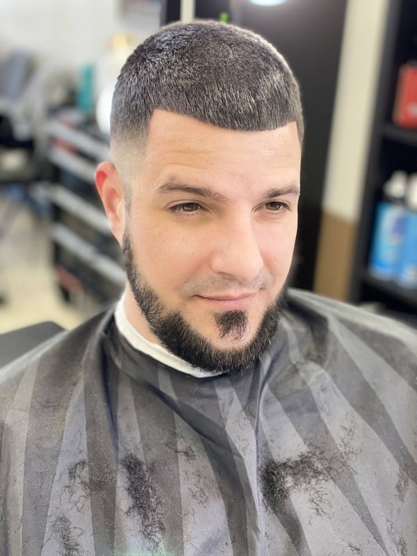 A client with a sharp mid fade and a shaped, lined-up beard.